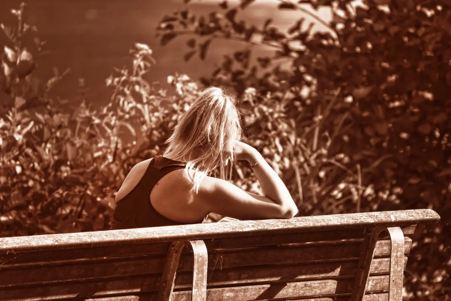 A woman sitting on top of a wooden bench.